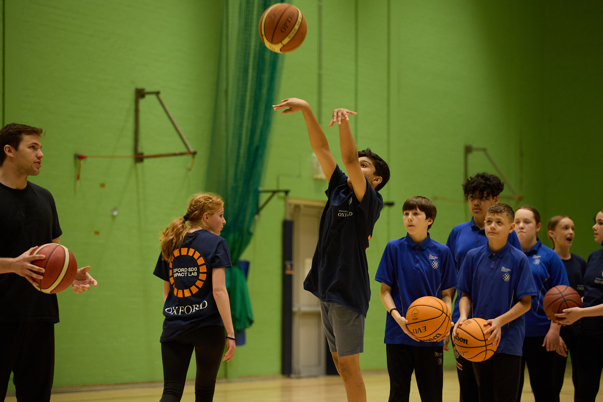 Pupil jumping up to shoot a hoop with queue waiting for their turn