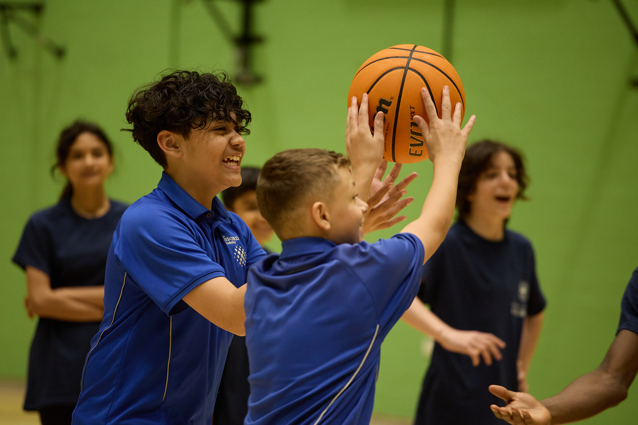 Pupils smiling reaching for ball in basketball practice