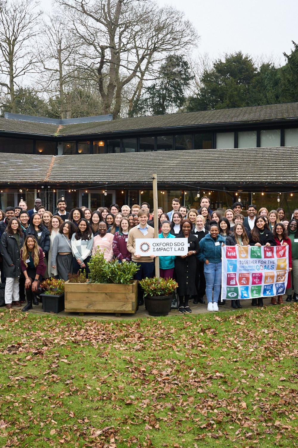 2025 Fellows Group Shot with SDG Flag and Lab Sign Outside Garden House