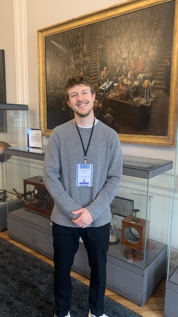 Miles Judd smiling to camera in a room with large painting behind him