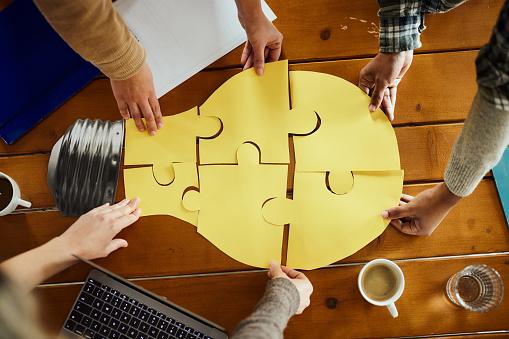 Hands joining together pieces of a jigsaw shaped like a lightbulb